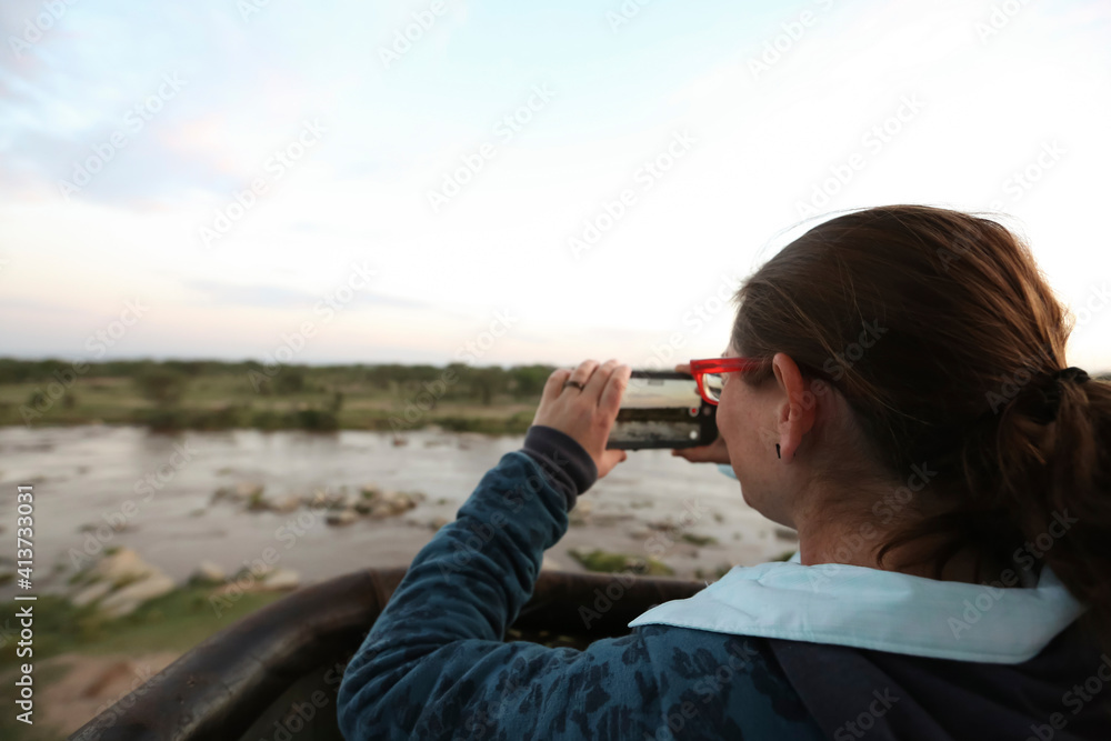 Rear view of woman photographing while standing at lakeshore against sky