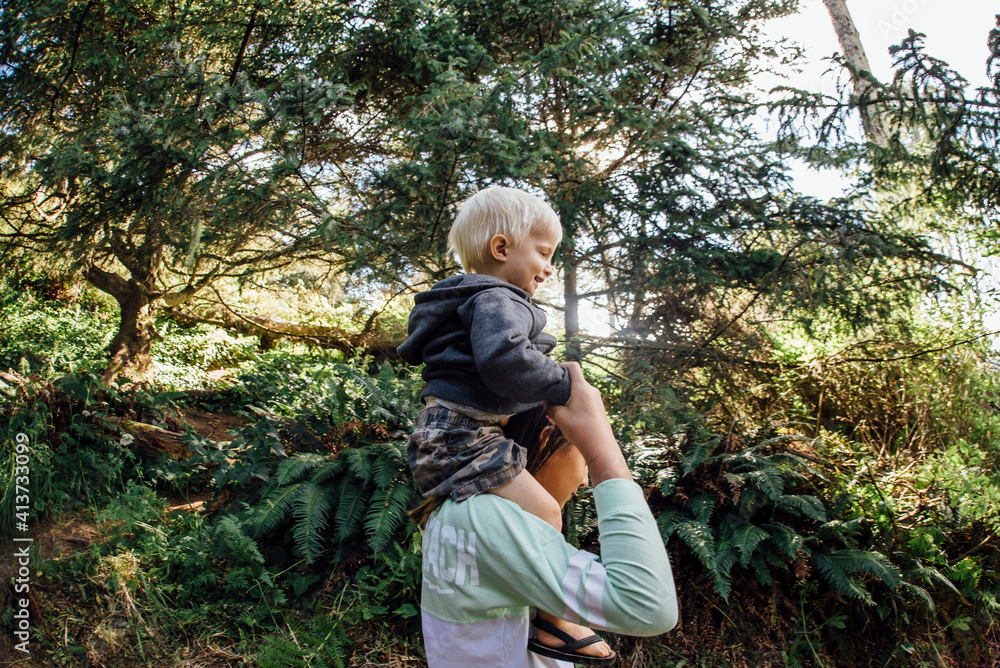 Side view of girl carrying brother on shoulders while standing by trees Side view of girl carrying brother on shoulders while standing by trees