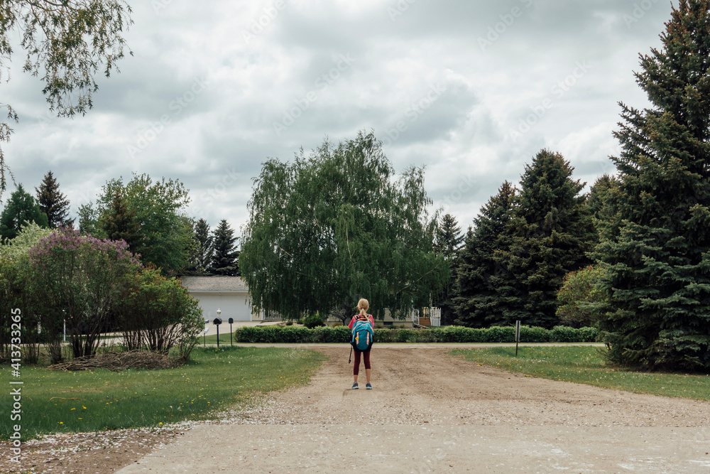 Rear view of girl with backpack standing on footpath against sky Rear view of girl with backpack standing on footpath against sky