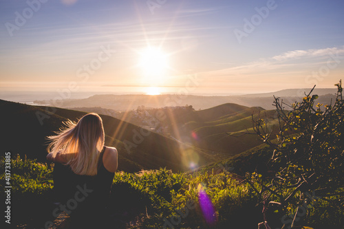 Rear view of woman sitting on mountain against sky during sunset photo