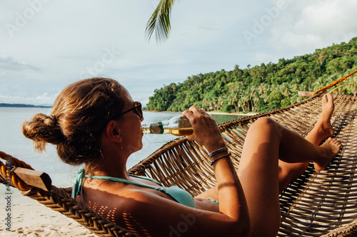 Young woman drinking alcohol while resting in hammock at beach photo