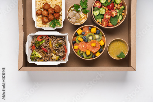 Cooked food in paper eco-friendly containers on white background. Food delivery for home or office. Vegetable, fruit salads, soups, meat and side dishes