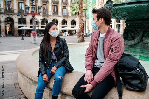 Two friends talking while wearing a face mask outdoors.
