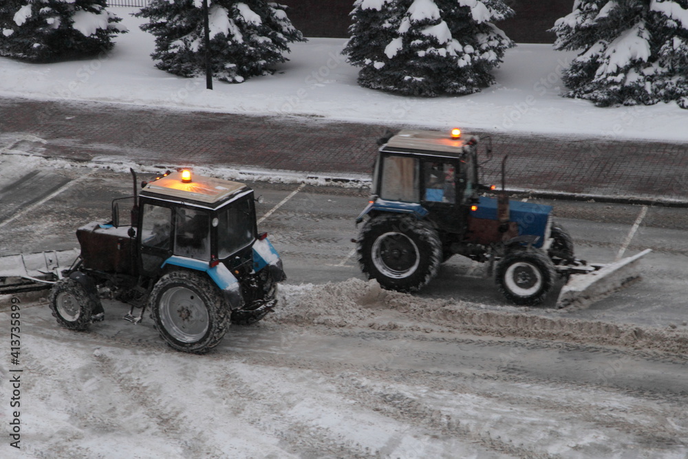 Wheeled traktors removes a snow cleaning on parking place after heavy snowfall at winter evening top side view Wheeled traktors removes a snow cleaning on parking place after heavy snowfall at winter evening top side view
