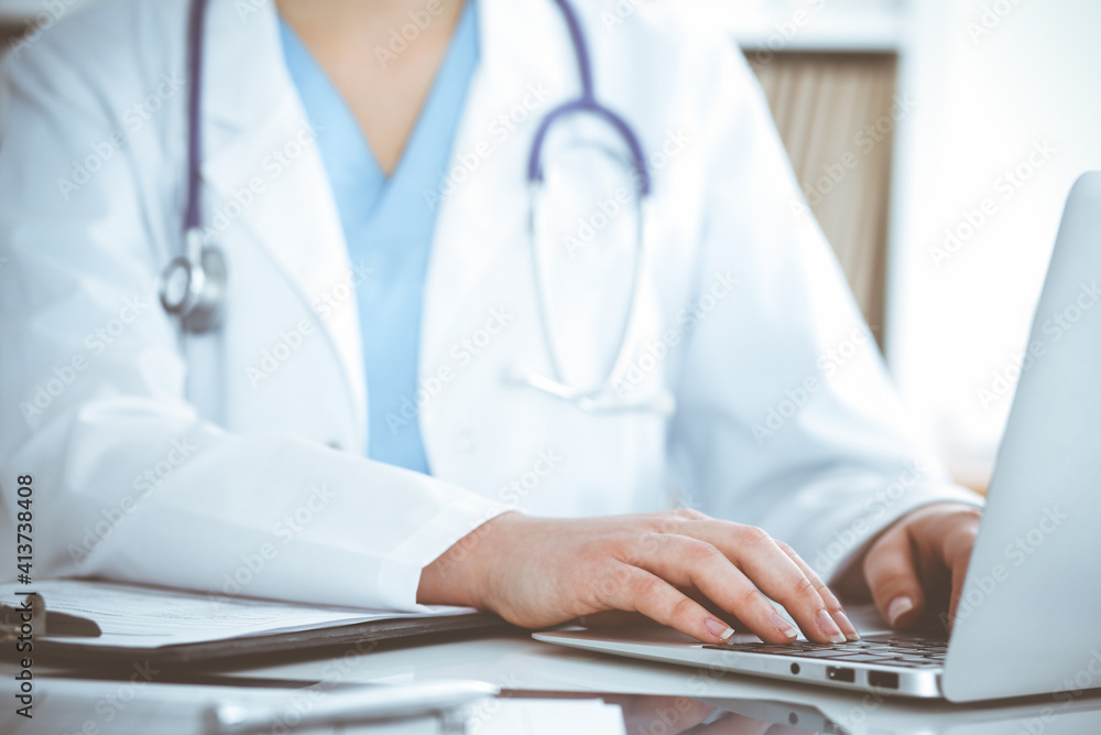 Unknown woman-doctor typing on laptop computer while sitting at the table. Medicine concept Unknown woman-doctor typing on laptop computer while sitting at the table. Medicine concept