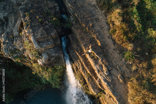 High angle view of woman with arms outstretched sitting over waterfall on mountain at forest photo