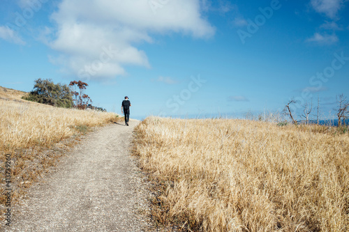 Rear view of hiker walking on road amidst plants against sky during sunny day photo