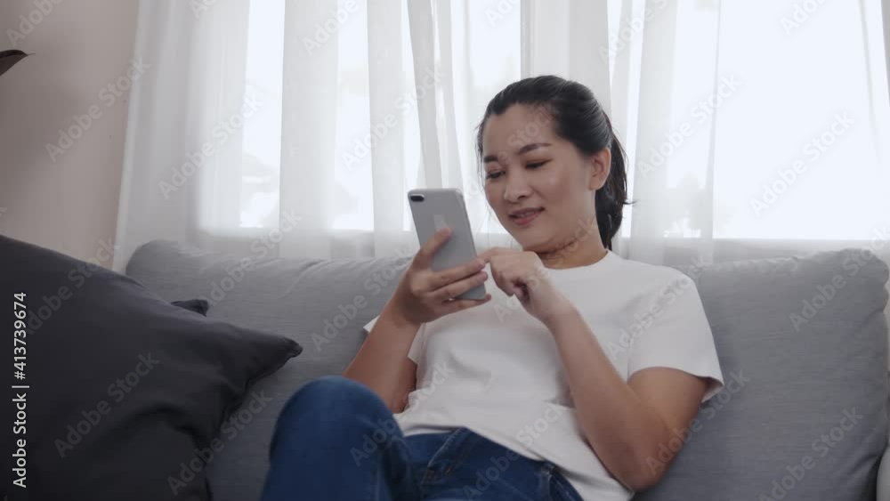 Young Asian woman using a smartphone for shopping online by application E-commerce is easy to sell or buy everything sitting on the sofa in the living room at home Young Asian woman using a smartphone for shopping online by application E-commerce is easy to sell or buy everything sitting on the sofa in the living room at home