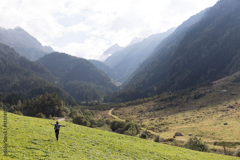 Rear view of female hiker running with arms outstretched on hill against mountains Rear view of female hiker running with arms outstretched on hill against mountains