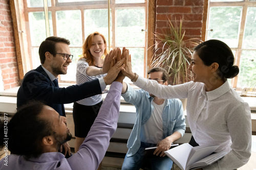 Excited diverse multiracial businesspeople give high five engaged in teambuilding activity at team office meeting. Happy multiethnic colleagues celebrate work result at briefing. Teamwork concept.