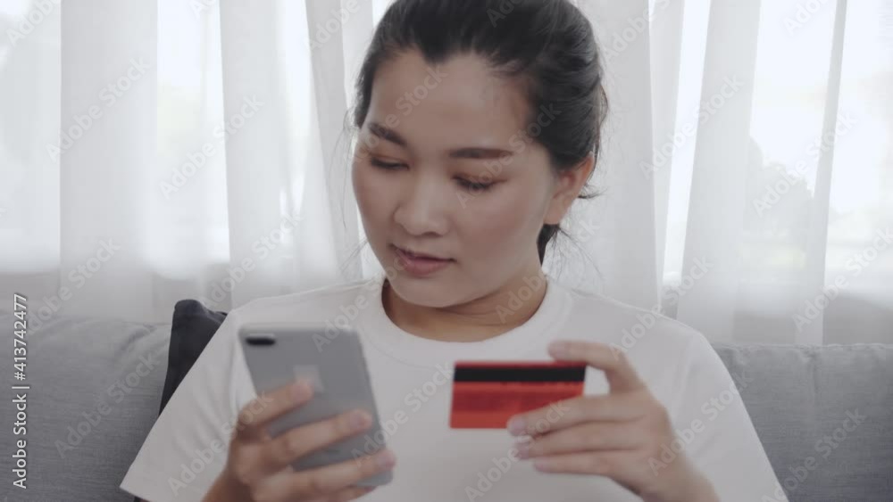 Happy Asian women shopping online and purchase by credit card on her smartphone for relax free time in the living room at home Happy Asian women shopping online and purchase by credit card on her smartphone for relax free time in the living room at home