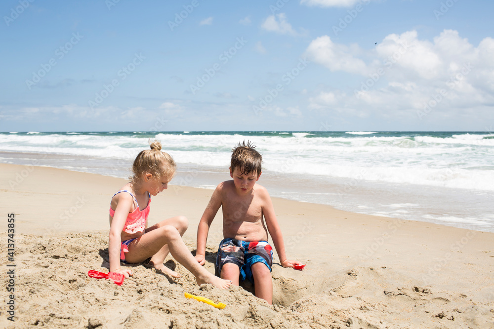 Siblings playing with sand at beach against sky during sunny day Siblings playing with sand at beach against sky during sunny day