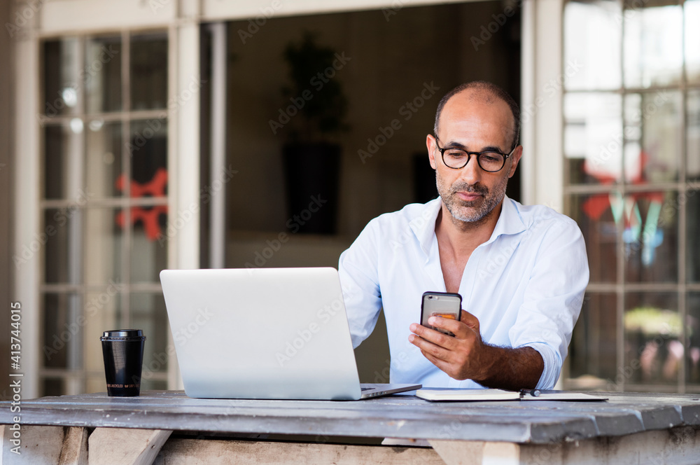 Businessman using smart phone while sitting with laptop computer at table in office Businessman using smart phone while sitting with laptop computer at table in office