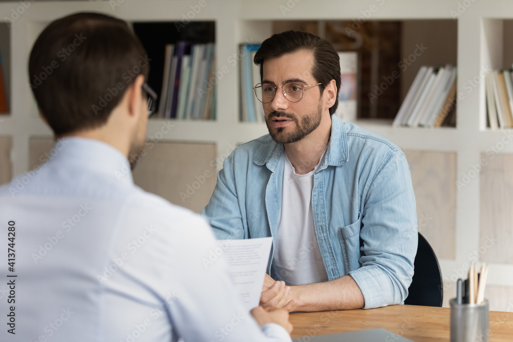 Young Caucasian male talk with employer or boss at job interview in office. Pensive serious millennial man candidate apply for vacant work position, speak with CEO or recruiter. Employment concept. Young Caucasian male talk with employer or boss at job interview in office. Pensive serious millennial man candidate apply for vacant work position, speak with CEO or recruiter. Employment concept.
