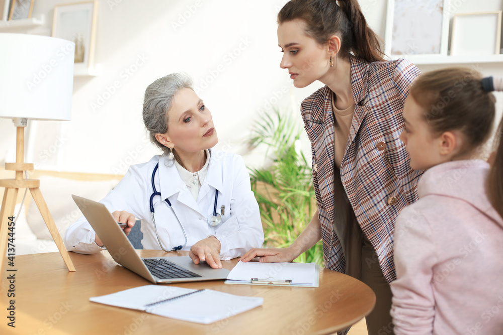 Mother and child in the doctor office meeting the pediatrician, they are sitting at desk in hospital.