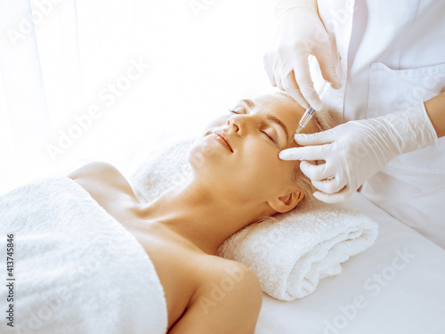 Beautician doctor hands doing beauty procedure to female blonde face with syringe in clinic. Cosmetic medicine and surgery, beauty injections concept