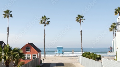 Colorful waterfront cottages, Oceanside California USA. Multicolor bungalow huts, summer sea, beachfront lodging. Many vacation houses on beach, ocean waves and palm trees. Lifeguard tower, watchtower © Dogora Sun