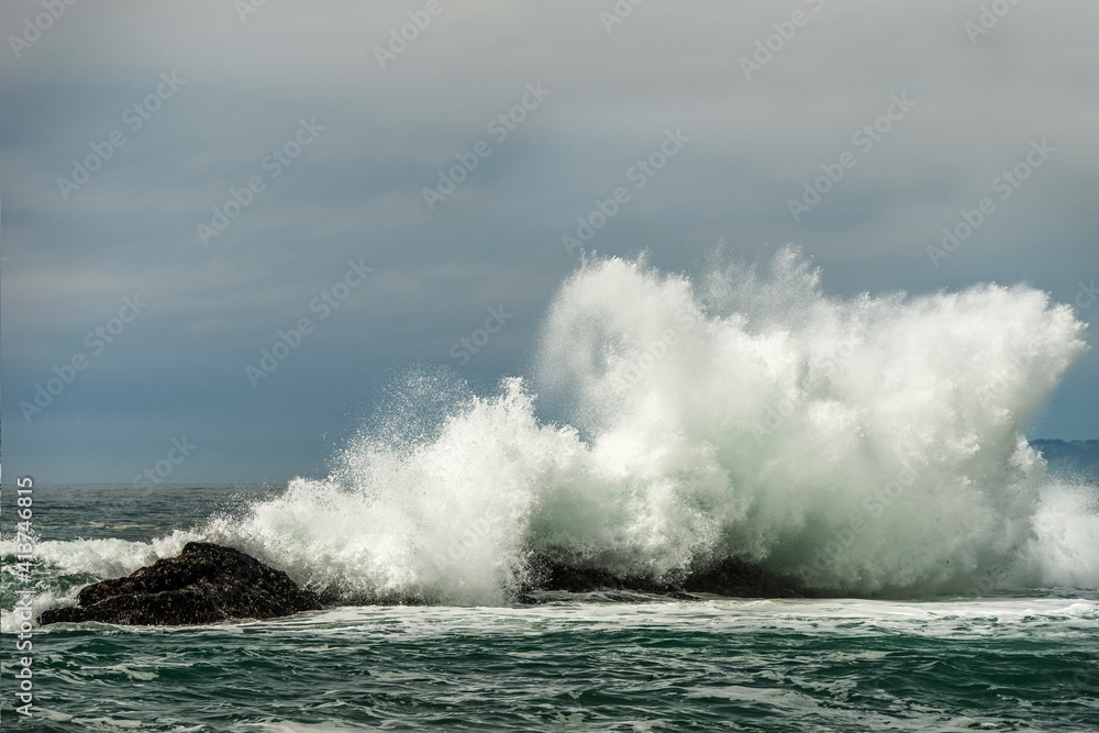 Waves splashing on rocks in sea against cloudy sky Waves splashing on rocks in sea against cloudy sky