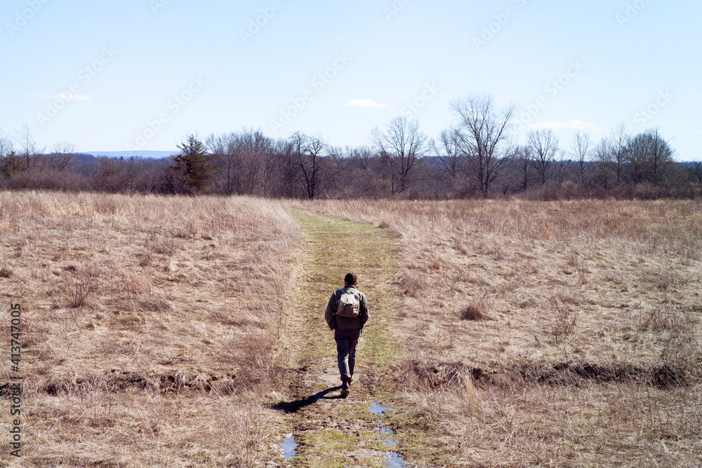 Rear view of male hiker walking on field during sunny day Rear view of male hiker walking on field during sunny day