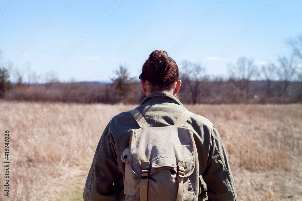 Rear view of male hiker carrying backpack while standing at field during sunny day Rear view of male hiker carrying backpack while standing at field during sunny day