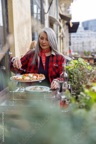 Beautiful matured asian woman is eating pizza in cafe terace