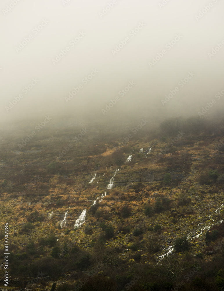 Scenic view of waterfall over mountain during foggy weather Scenic view of waterfall over mountain during foggy weather
