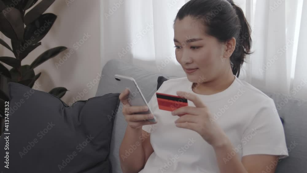 Happy Asian women shopping online and purchase by credit card on her smartphone for relax free time in the living room at home Happy Asian women shopping online and purchase by credit card on her smartphone for relax free time in the living room at home