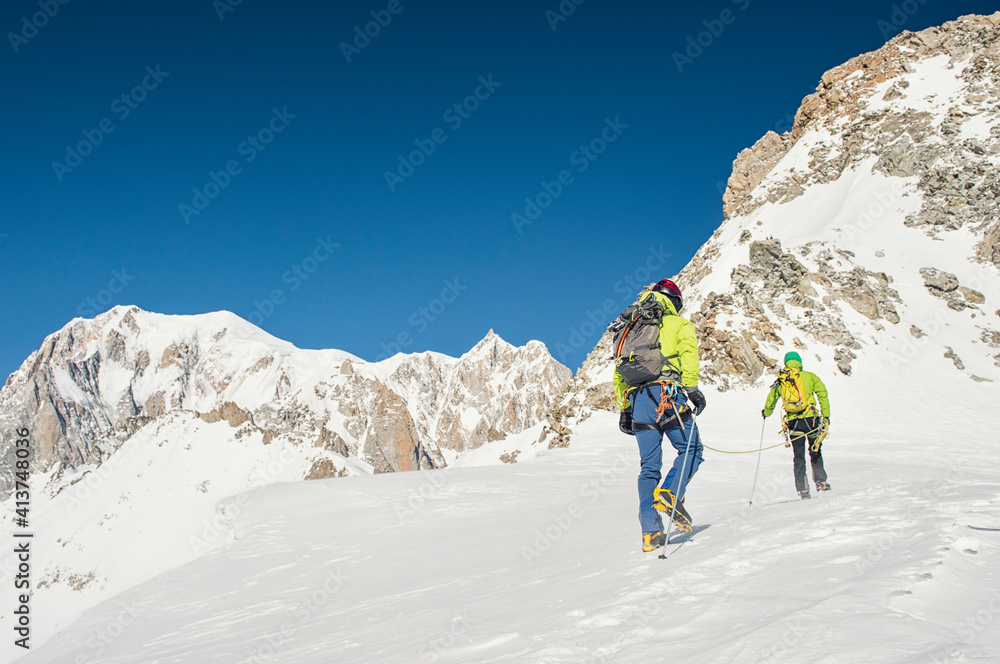Rear view of hikers with backpacks climbing mountain against clear blue sky during sunny day Rear view of hikers with backpacks climbing mountain against clear blue sky during sunny day