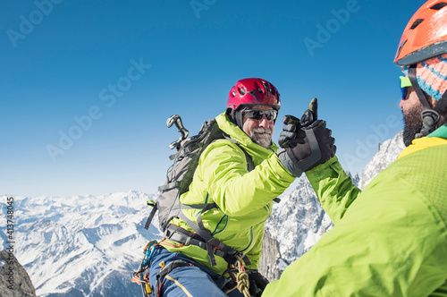 Hiker assisting friend in climbing mountain against clear blue sky during winter