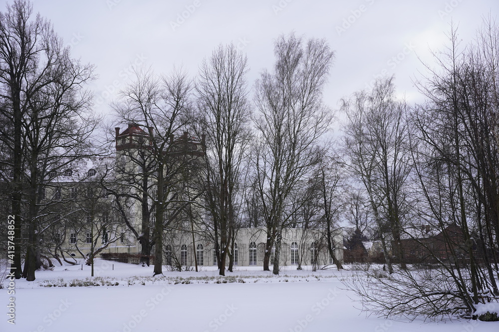 Fototapeta premium Schlosspark Lübbenau im Winter mit Schnee und Schloss hinter Bäumen