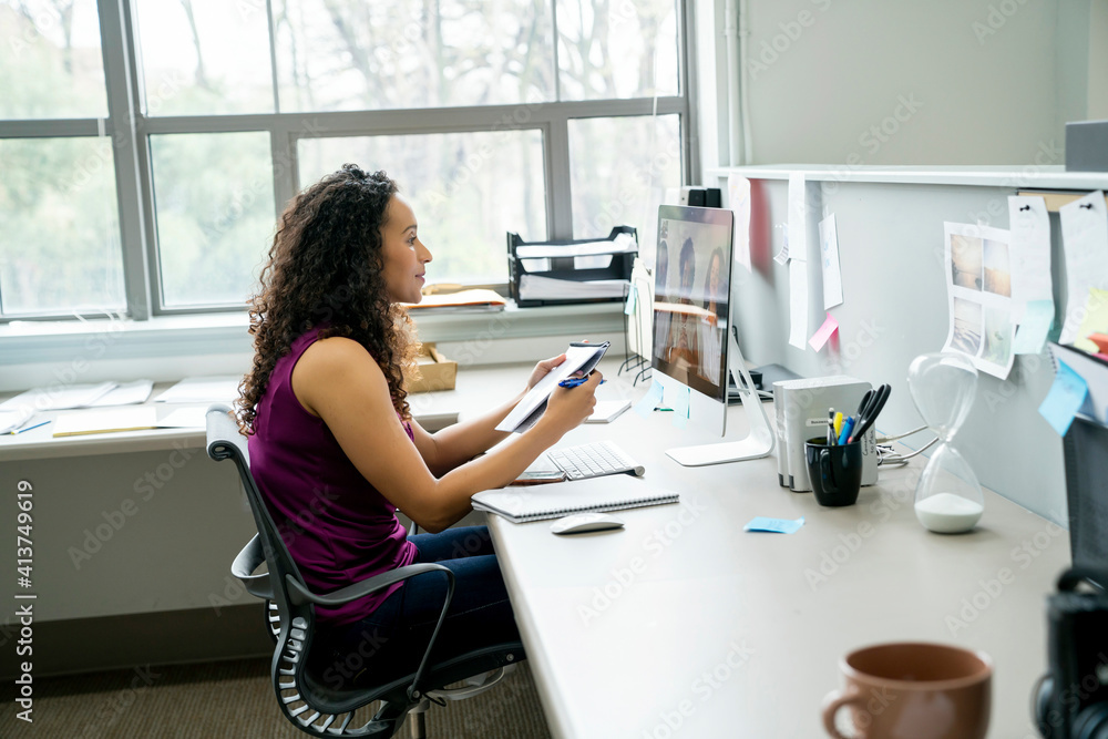 Side view of businesswoman discussing with coworkers video conferencing with colleague over desktop computer in office Side view of businesswoman discussing with coworkers video conferencing with colleague over desktop computer in office