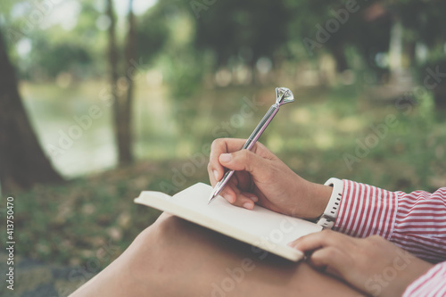 Woman hand writing down in small white memo notebook for take a note not to forget or to do list.