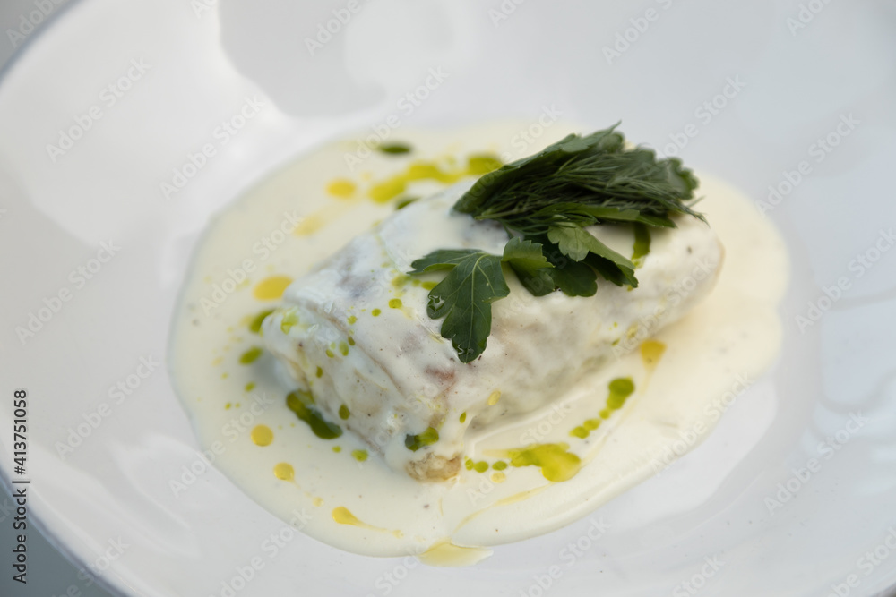 Scalding hot baked cabbage rolls with cream sauce close-up. Restaurant serving of cabbage rolls on a plate with greens. Scalding hot baked cabbage rolls with cream sauce close-up. Restaurant serving of cabbage rolls on a plate with greens.