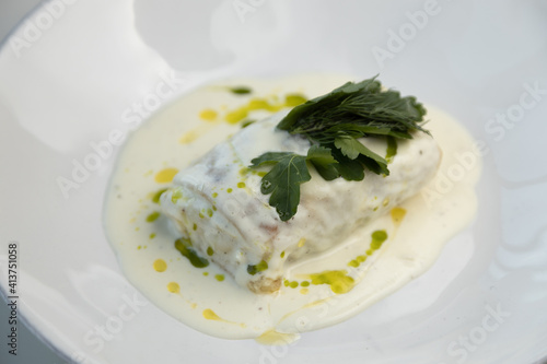 Scalding hot baked cabbage rolls with cream sauce close-up. Restaurant serving of cabbage rolls on a plate with greens.