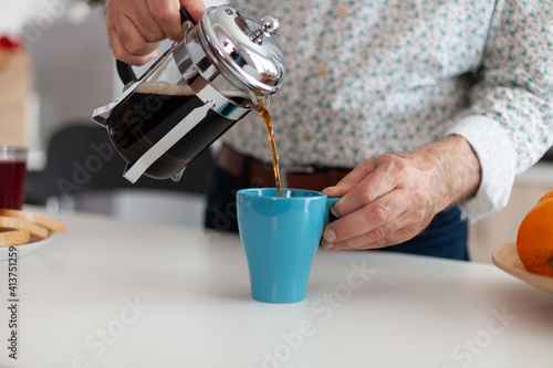 Elderly man using french press for coffee preparation and pouring it in mug. Senior person in the morning enjoying fresh brown cafe espresso cup caffeine from vintage mug, filter relax refreshment