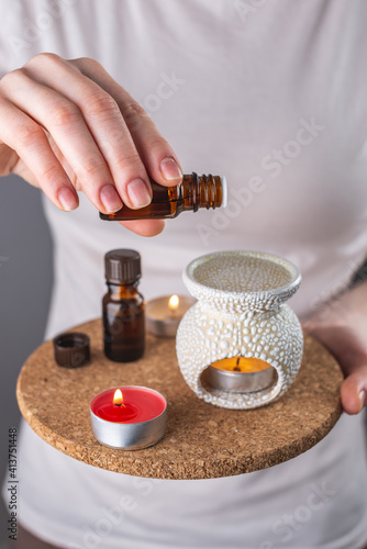 A woman is dripping organic essential oil into an aroma lamp for a relaxing and pleasant aromatherapy procedure. Closeup