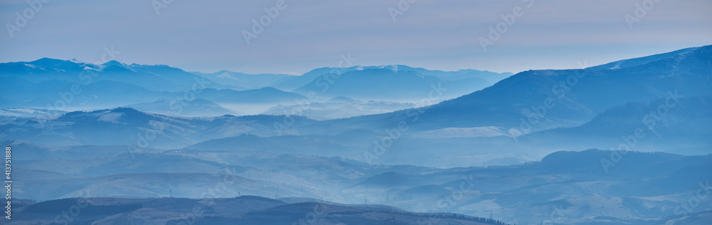 Mountain landscape in late autumn. The blue silhouettes of the mountains hide in a white haze. Nature falls asleep