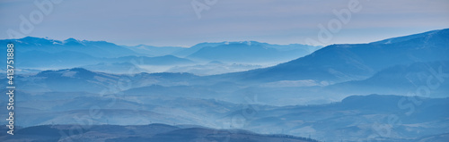 Mountain landscape in late autumn. The blue silhouettes of the mountains hide in a white haze. Nature falls asleep