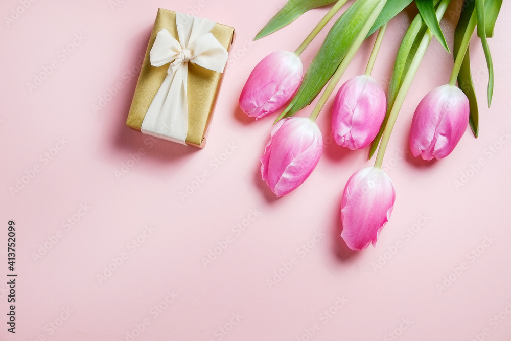Multipurpose fresh flower composition, bouquet of pink tulips and a present wrapped in golden paper. International Women's day greeting concept. Copy space, close up, top view, flat lay, background.