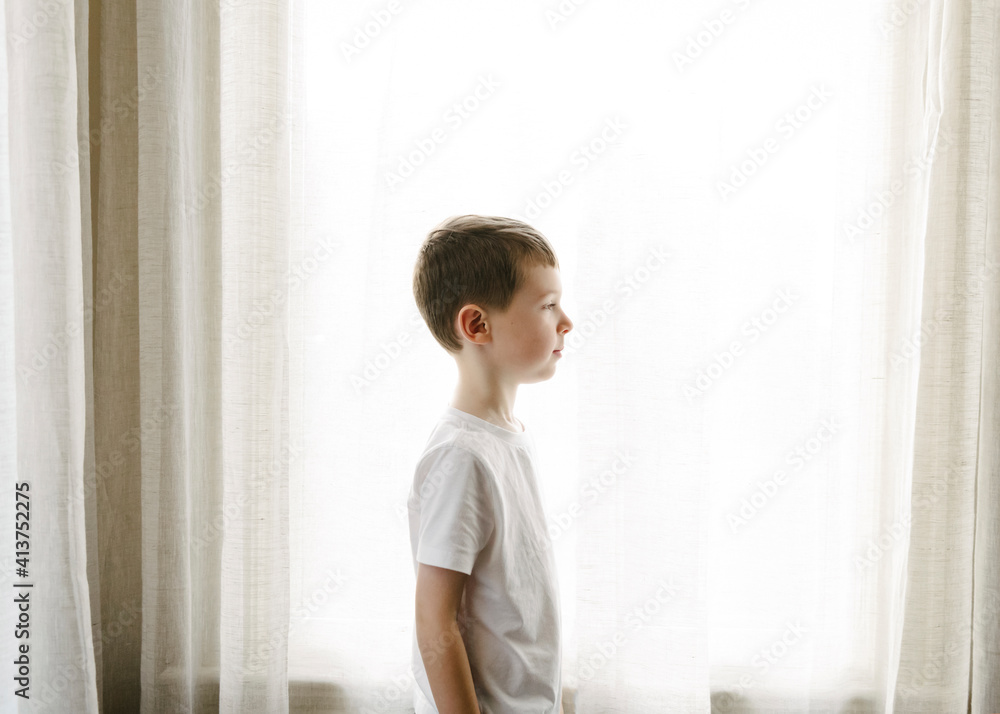 Side view of boy standing against curtains at home Side view of boy standing against curtains at home