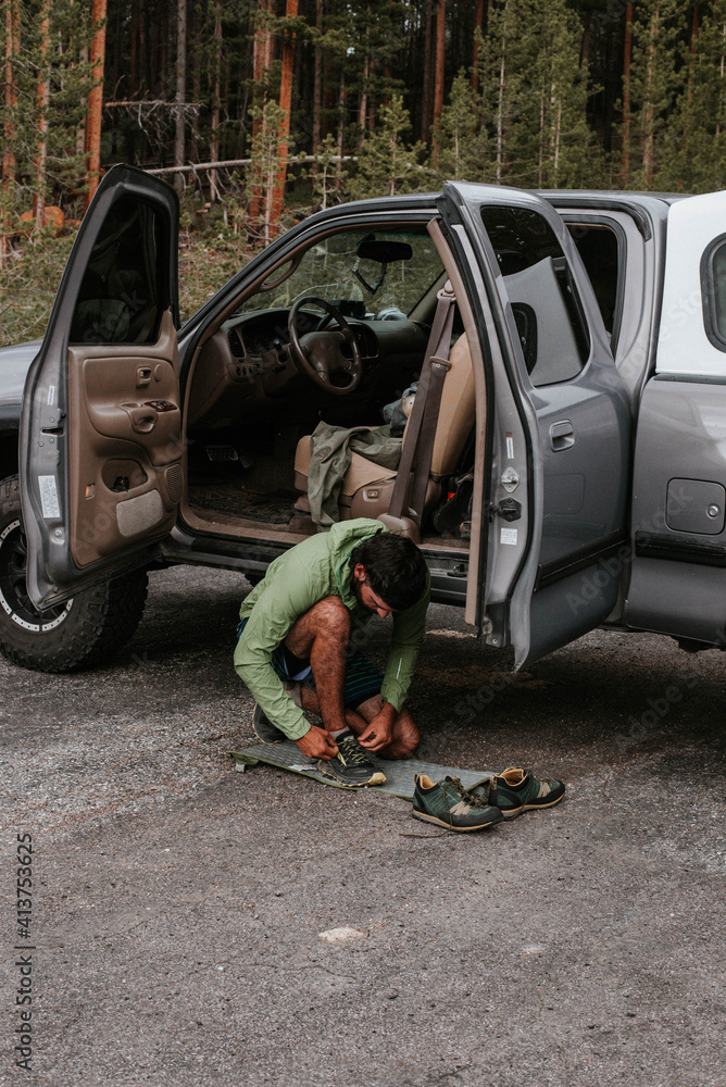 Hiker tying shoelaces while kneeling against car on road at Arches National Park Hiker tying shoelaces while kneeling against car on road at Arches National Park