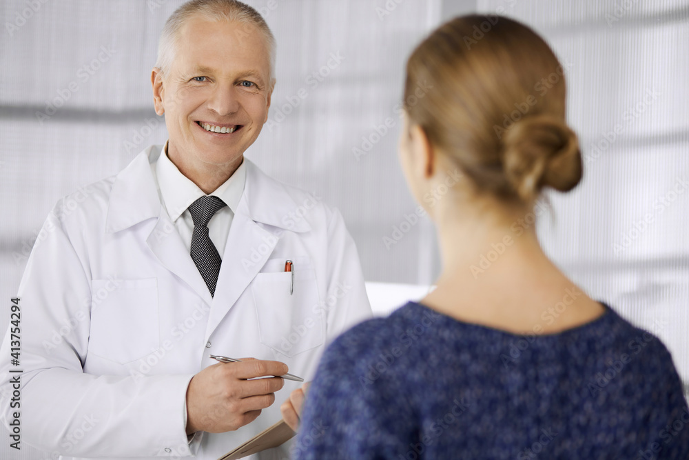 Elderly confident doctor consults woman patient in clinic. Perfect medical service in hospital. Medicine and healthcare concept Elderly confident doctor consults woman patient in clinic. Perfect medical service in hospital. Medicine and healthcare concept