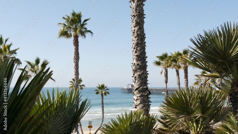 Pacific ocean beach, green palm trees and pier. Sunny day, tropical waterfront resort. Vista viewpoint in Oceanside, near Los Angeles California USA. Summer sea coast aesthetic, seascape and blue sky.