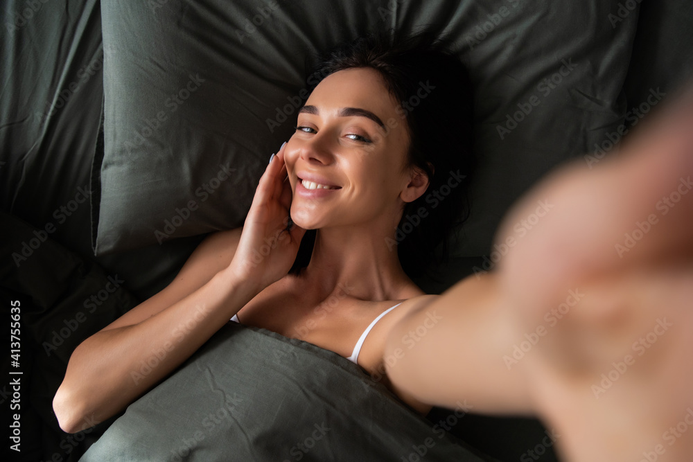 Beautiful funny young woman indoors at home make selfie by camera lies in bed. Beautiful funny young woman indoors at home make selfie by camera lies in bed.