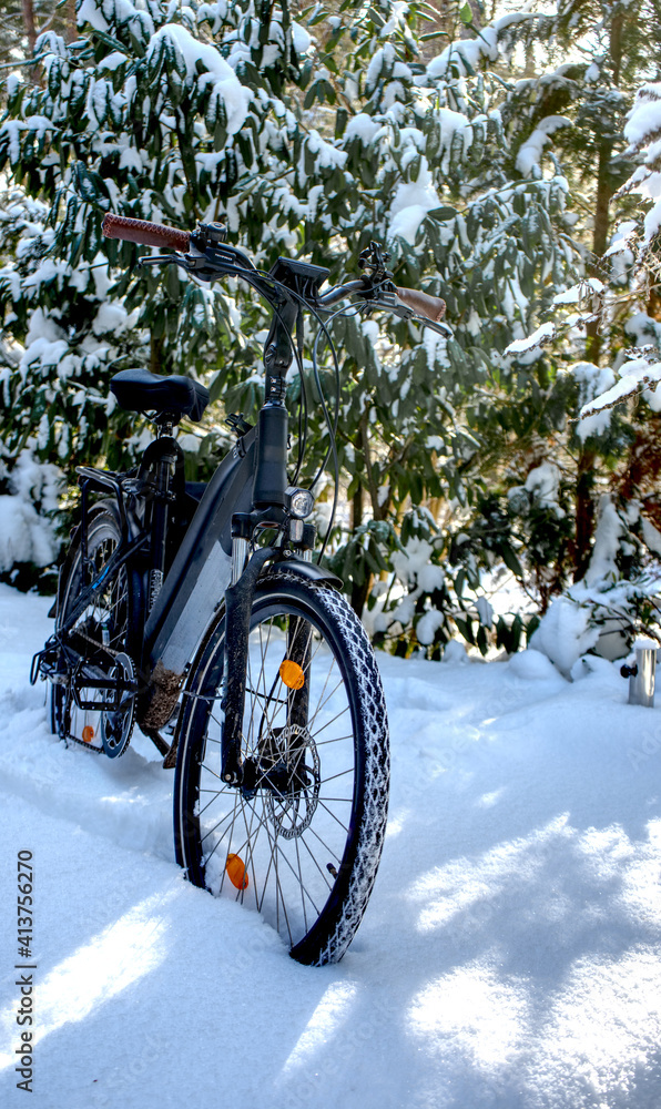 Black bike in deep dense white snow of winter with laurel bushes in background before bike ride in cold weather Black bike in deep dense white snow of winter with laurel bushes in background before bike ride in cold weather