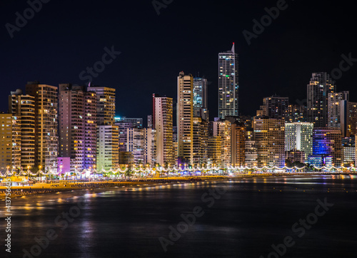 Night skyline of Benidorm with many lights from the skyscrapers lighting the beach, the coast and the Mediterranean sea when arrives o the shore. Horizontal picture photo