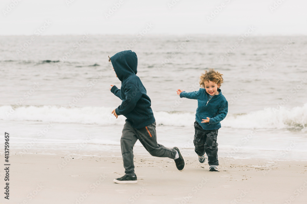 Happy brothers playing at beach against sky Happy brothers playing at beach against sky
