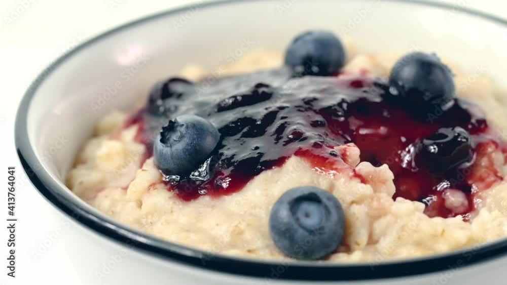 hand with a spoon takes a healthy freshly cooked oatmeal porridge with jam and fresh blueberries from a breakfast bowl close - up. home cooking hand with a spoon takes a healthy freshly cooked oatmeal porridge with jam and fresh blueberries from a breakfast bowl close - up. home cooking