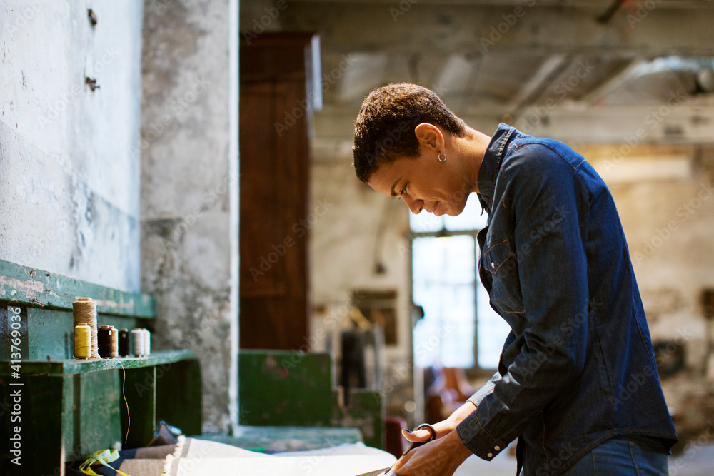 Side view of smiling designer cutting fabric in workshop