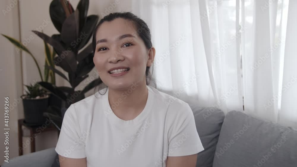 Happy Asian young female sitting on sofa talking to camera for communication to viewers shooting vlog and video, smiling ethnic girl greeting talking having a conversation or video call at home Happy Asian young female sitting on sofa talking to camera for communication to viewers shooting vlog and video, smiling ethnic girl greeting talking having a conversation or video call at home